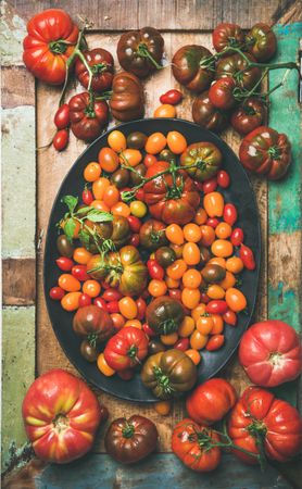 Assortment of different tomatoes in oval bowl, on wooden table, vertical composition