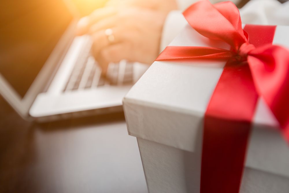 Gift Box with Red Ribbon and Bow Near Man Typing on Laptop Computer.