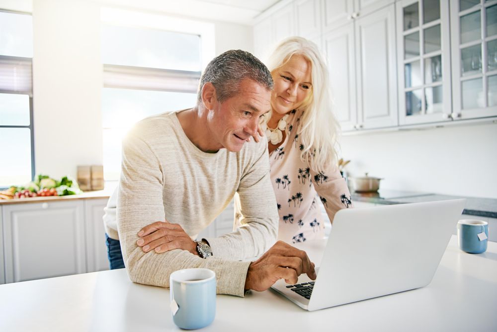 Older couple on a video call on their laptop in kitchen with tea