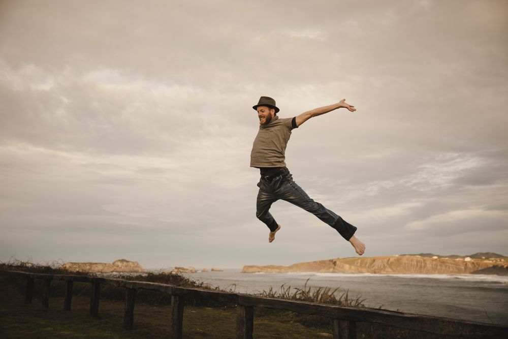 Young man in hats having fun on seat on coast near waving sea and cloudy sky