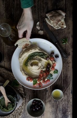 Crop hand dipping flatbread into hummus pesto with tomatoes and beans