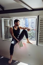 Young male sitting on window and reading book
