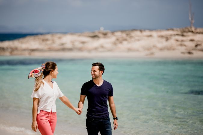 Happy couple walking on turquoise seashore in summer light
