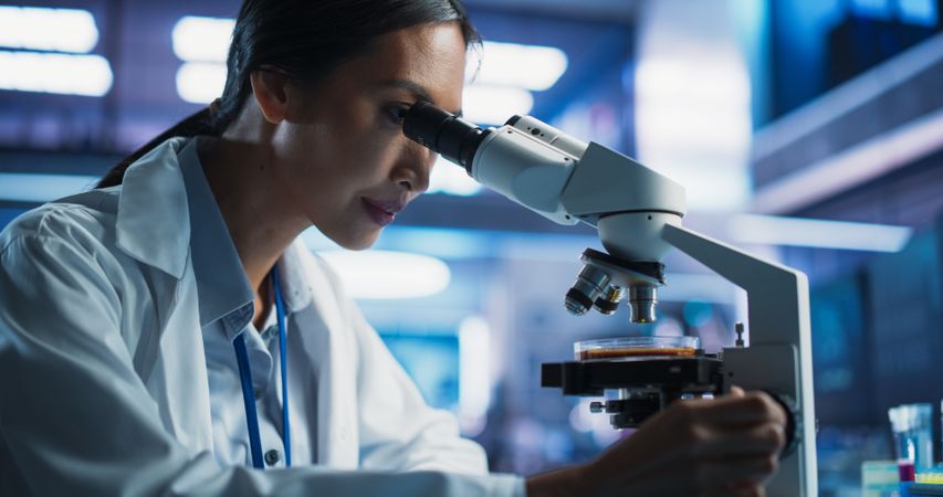 Medical Development Laboratory: Close-Up Portrait of Asian Female Scientist Using Microscope, Analyzes Petri Dish Sample.