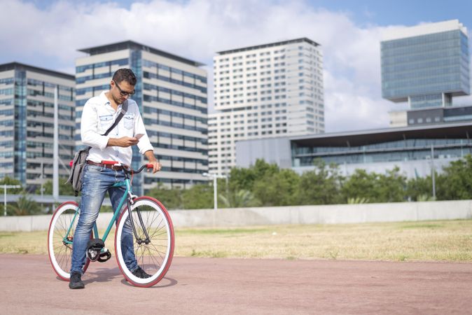 Male with colorful bicycle texting on phone on city bike path