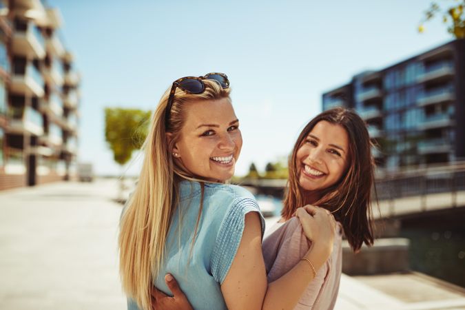 Two female friends looking back and smiling along the river on a sunny day