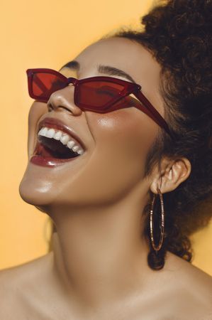 Woman wearing red sunglasses and gold-colored hoop earring smiling