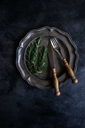 Table setting with dark plate with rosemary sprig