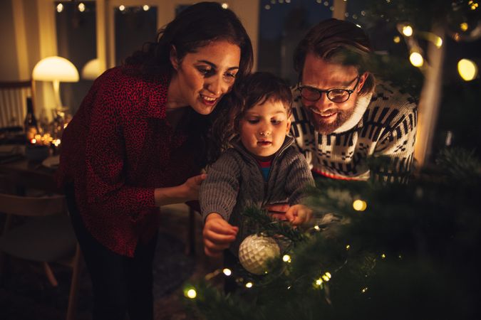 Boy tying decorative balls on Christmas tree with parents at home
