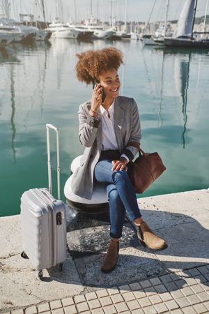 Black woman with luggage talking on smartphone in port