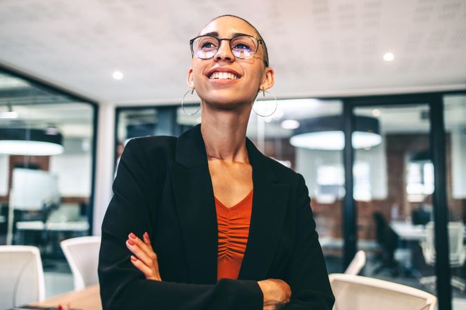 Woman with shaved head standing with arms crossed smiling in office boardroom