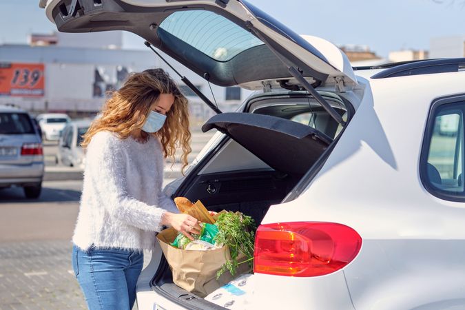 Woman in face mask placing shopping bags in car trunk