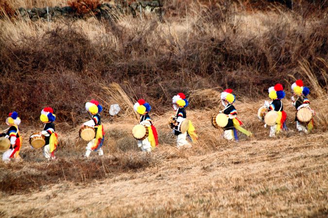 Men in multi-colored wig playing drums walking in yellow grass field