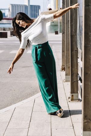 smiling young woman hanging on a pole in the street while looking down