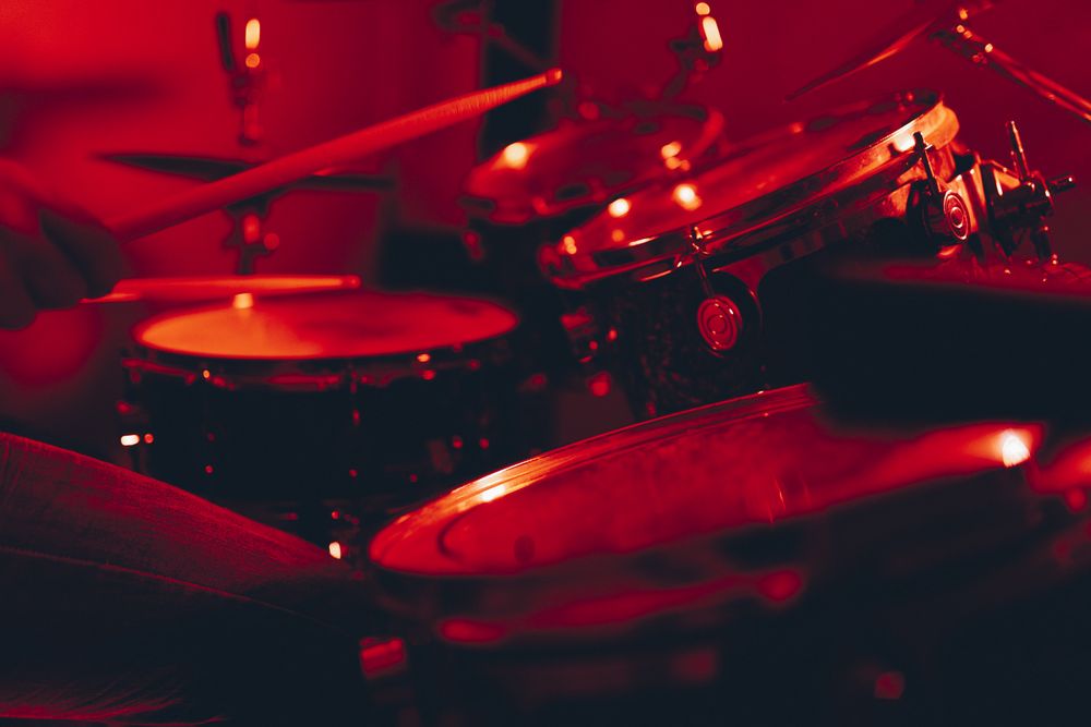 Anonymous man with drumsticks playing on drums in redness