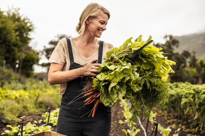 Cheerful farmer holding freshly picked organic vegetables in an agricultural field