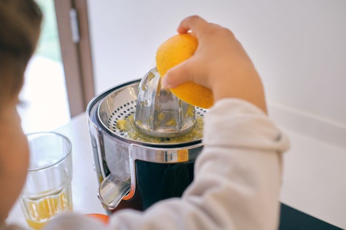 Crop child making fresh orange juice in kitchen