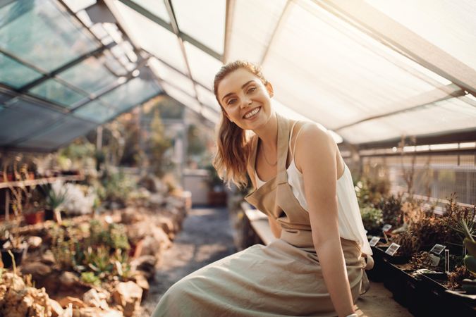 Portrait of smiling woman sitting in greenhouse