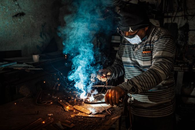 Blue smoke rises as a man welds metal