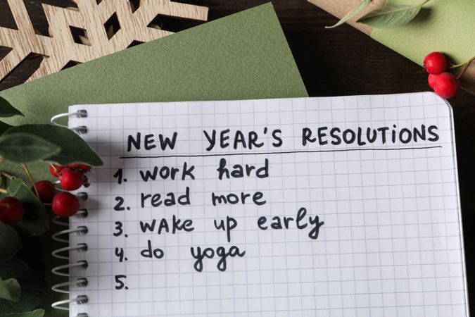 Notepad with list and decorations on wooden background, top view