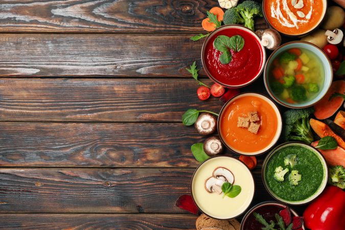 Top view of colorful soups on dark wooden table with copy space