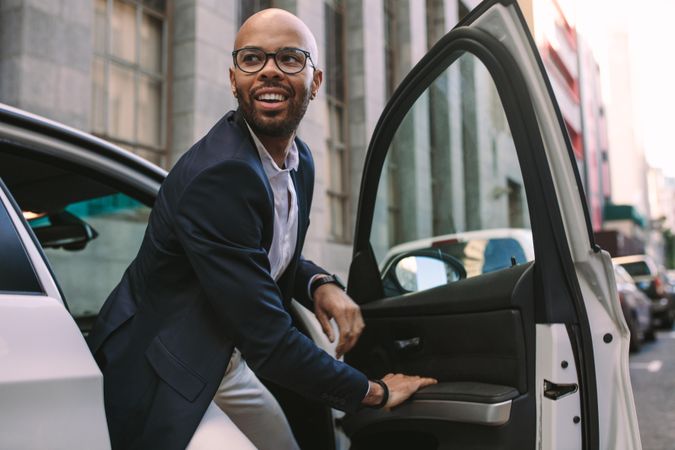 Happy young businessman getting out of car on road