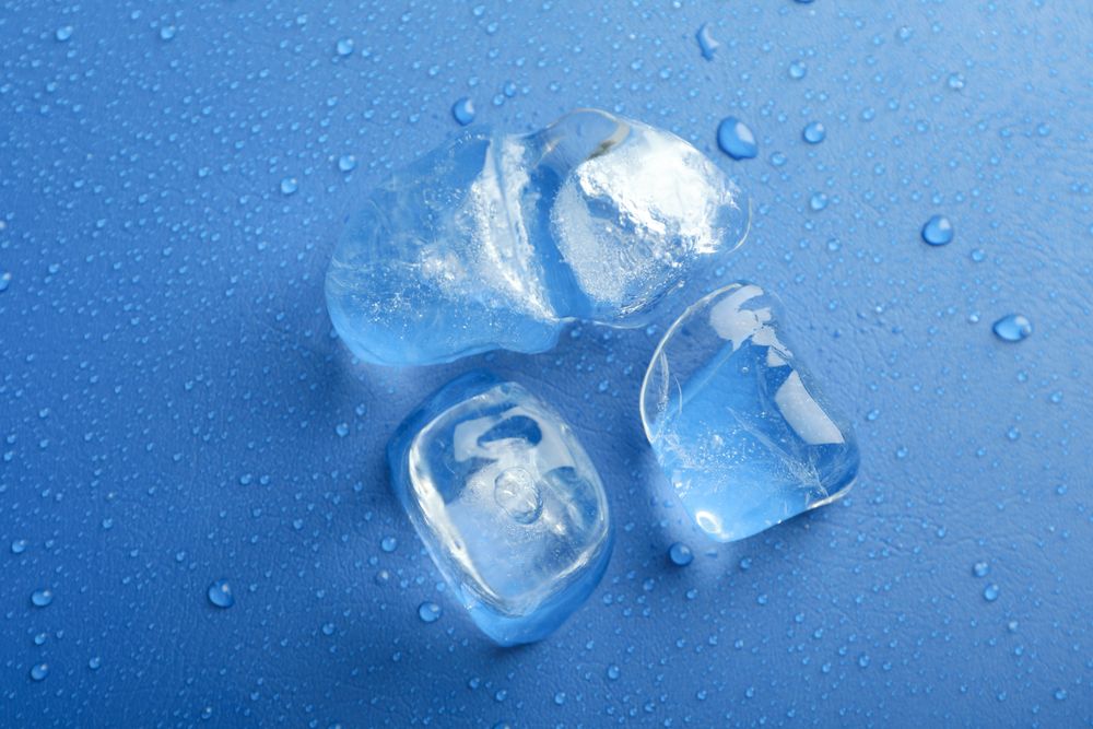 Looking down at top view of four melting ice cubed on blue table