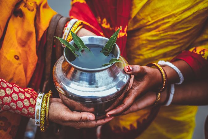 Cropped image of Indian women wearing saris holding a metal jar with herbs