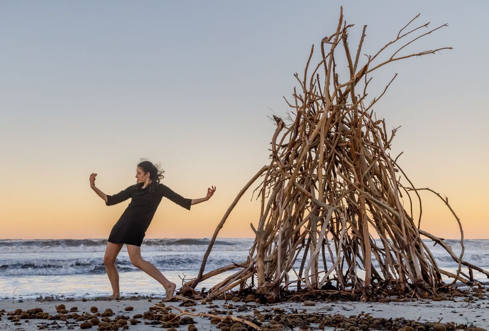 Young woman dancing on shore near water and wooden twigs placed for campfire