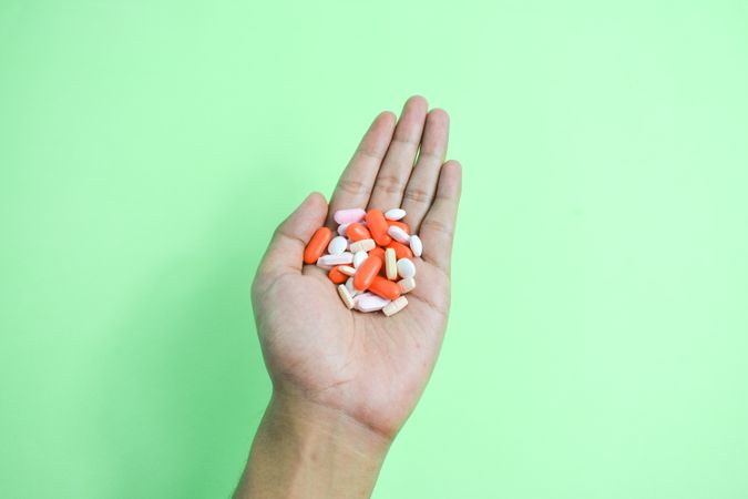Hand holding variety of colorful medication and vitamins in center of green table