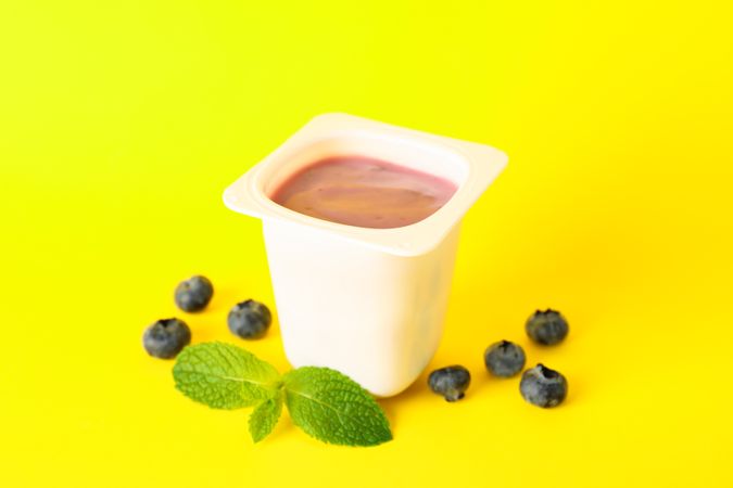 Plastic cup with yogurt on color background, space for text