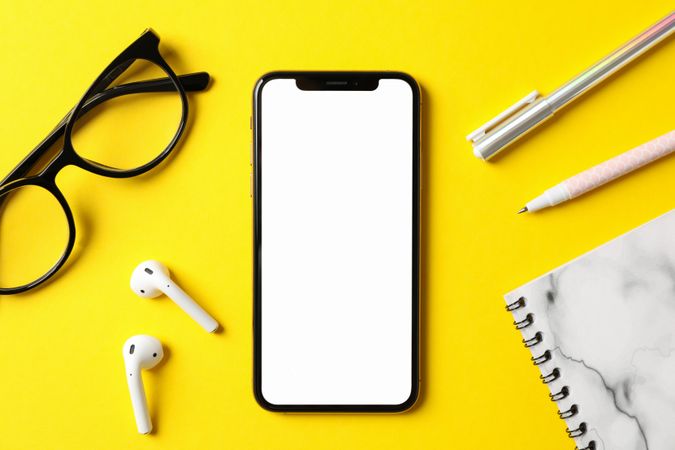 Workplace with phone with empty screen, top view