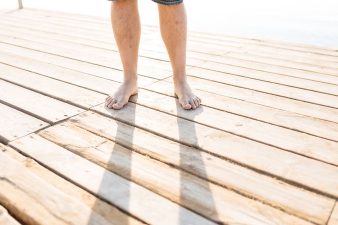 Legs of adult standing on wooden pier in sunlight
