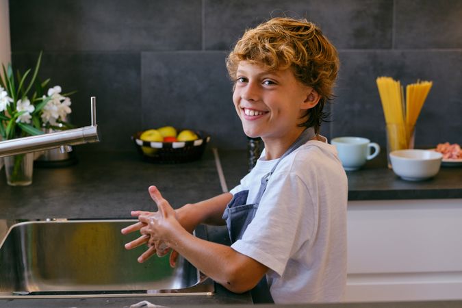 Smiling boy washing hands over sink in kitchen