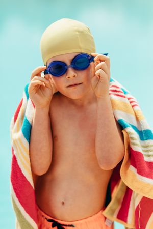 Cute little boy wrapped in towel standing by pool