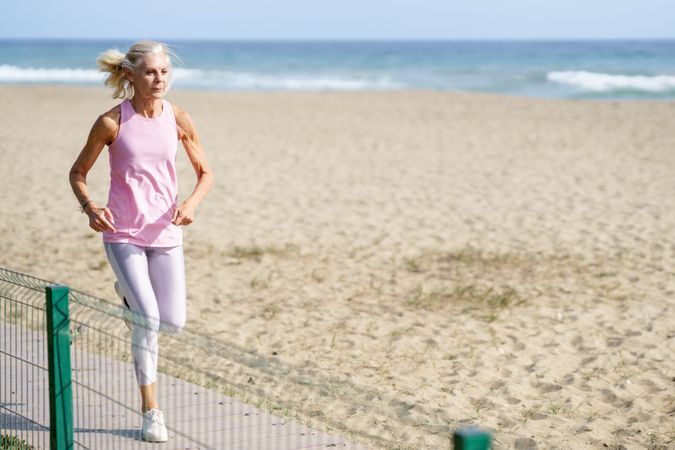 Healthy older woman in sports gear running along beach