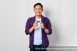 Happy Asian male in grey studio holding up credit card with his hands 4Mepa4