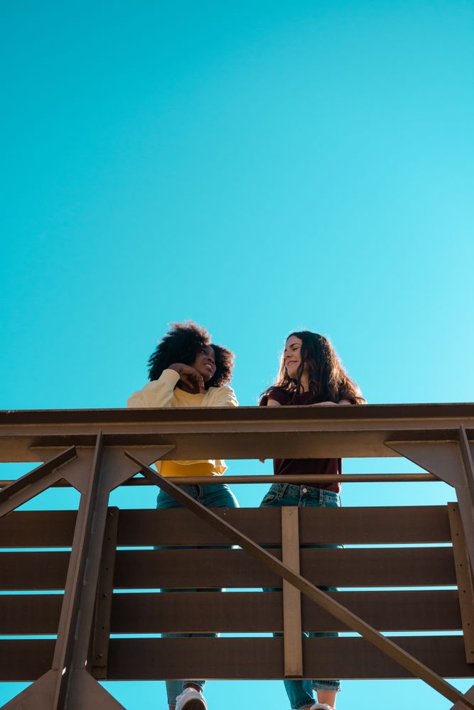 Two females talking on a bridge.