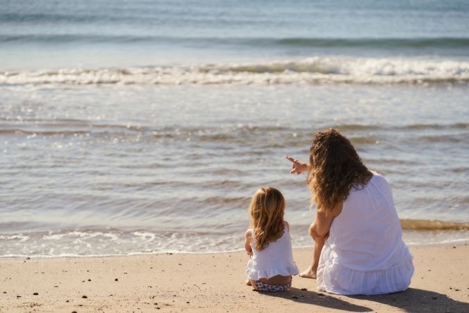 Mother and child sitting on the beach looking at the sea. back view