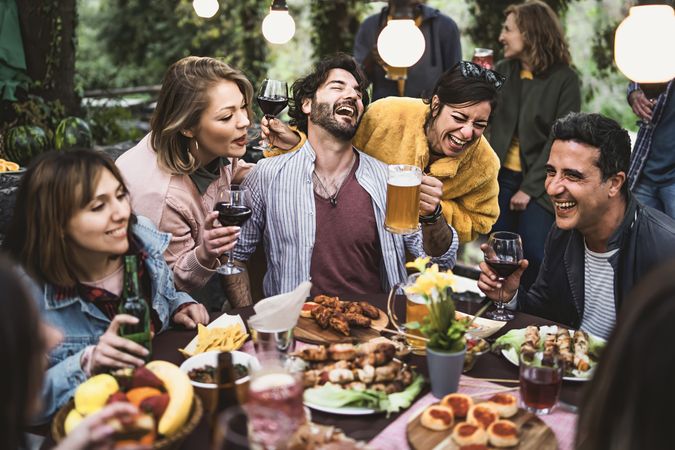 Group of hilarious friends have fun drinking beer and wine and eating together on the weekend at the restaurant table in the countryside