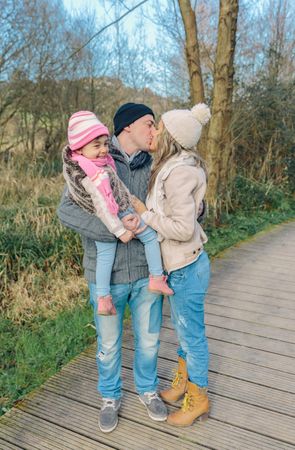 Father holding daughter a he kisses wife, vertical composition