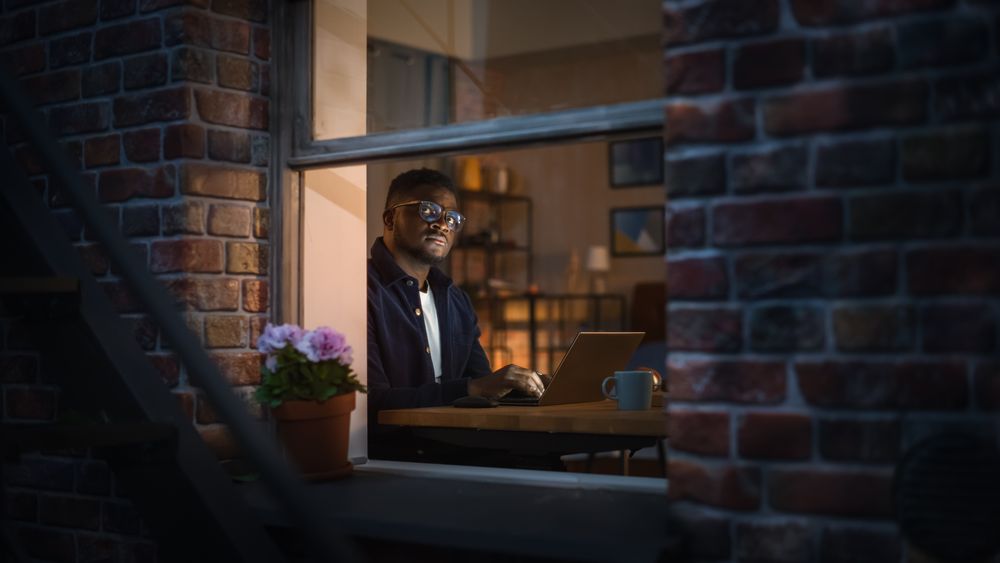 Portrait of Black Productive Young Man Working on Laptop from Home on Bedroom Desk.