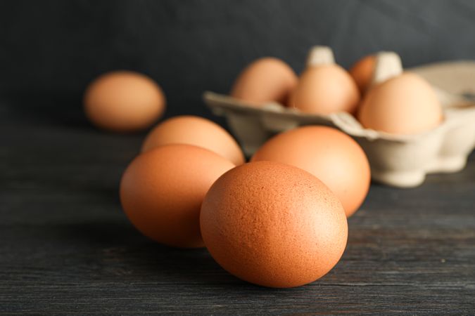 Brown chicken eggs in carton box on wooden table against dark background, space for text and closeup