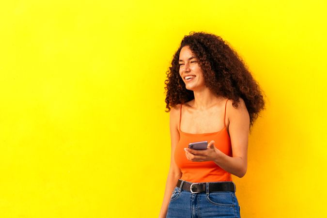 young afro latina woman using her mobile leaning on a yellow wall