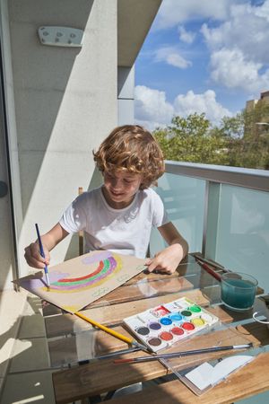 Cheerful boy drawing rainbow on terrace