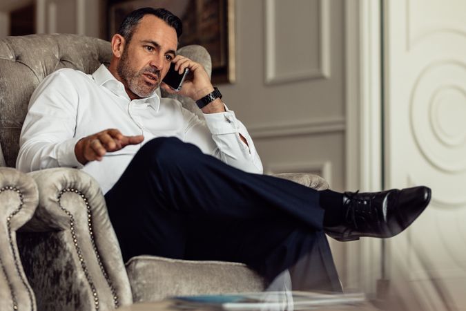 Businessman sitting on couch and talking on smartphone