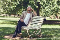 Portrait of a mature man, sitting on bench in a park 4mqYX4
