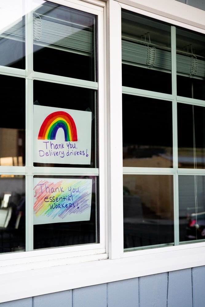 Two handmade signs taped inside of house window thanking delivery drivers and essential workers