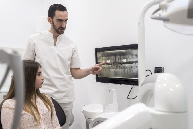 Attractive young dentist showing to female patient xray of her teeth