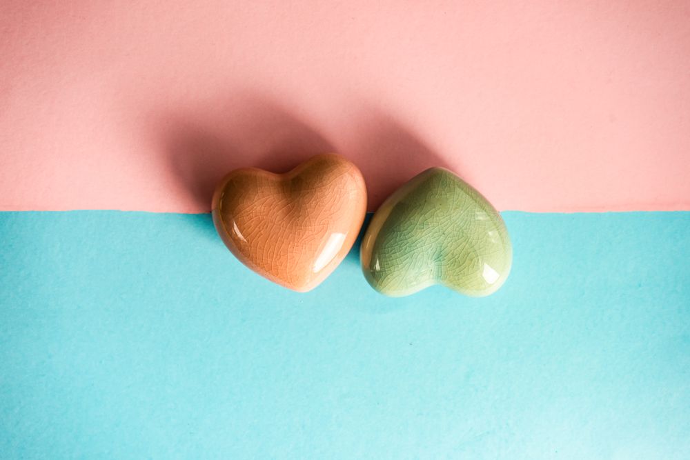 Orange and green heart ornaments on blue and pink pastel background 